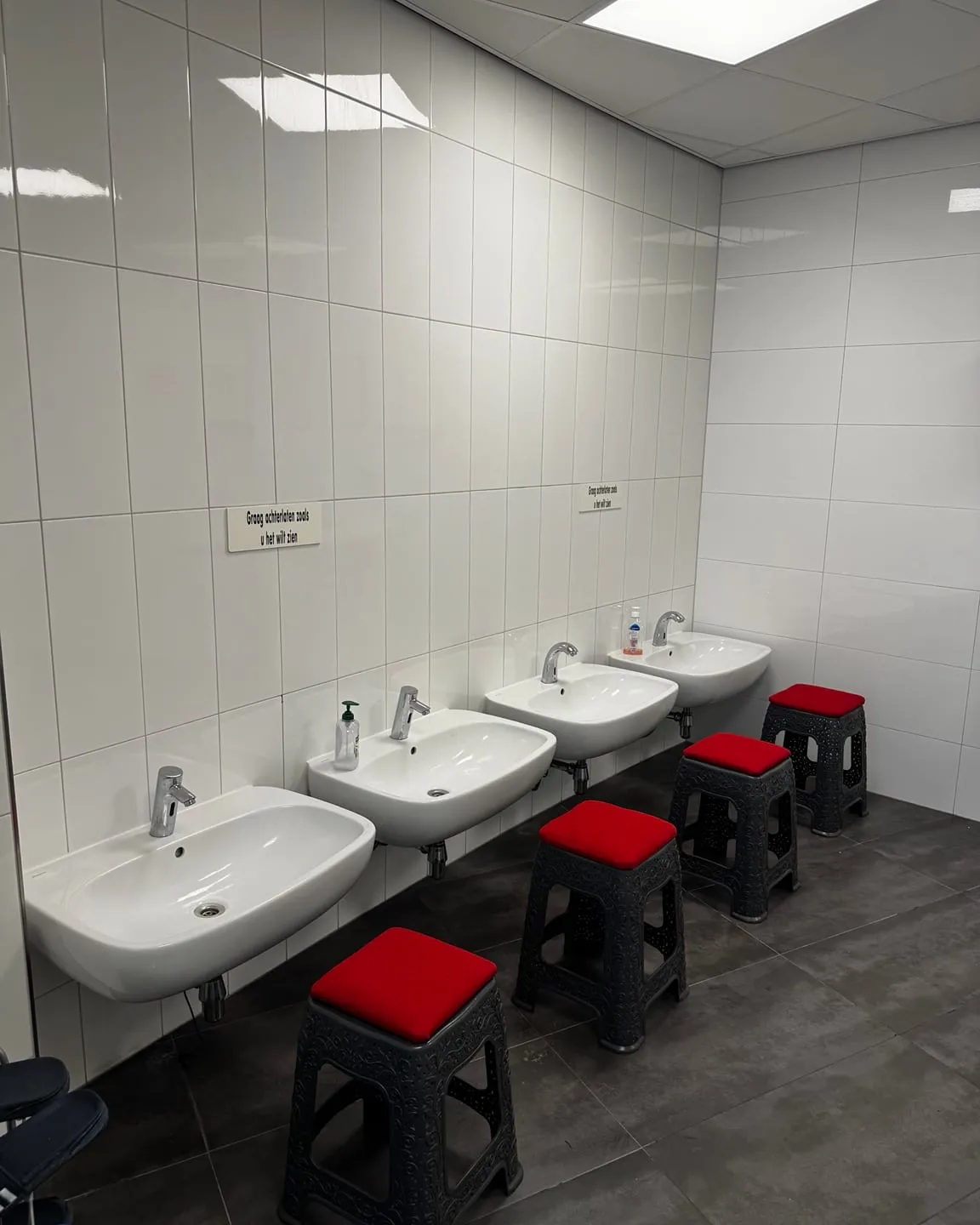 Een rij witte wastafels op een lijn gemonteerd tegen een betegelde wand