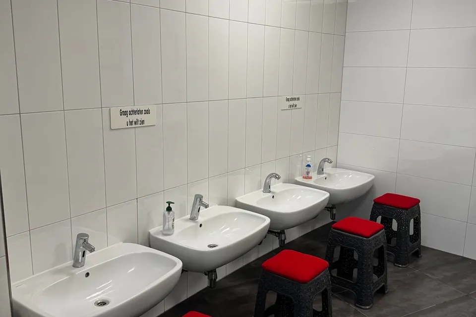 Een rij witte wastafels op een lijn gemonteerd tegen een betegelde wand