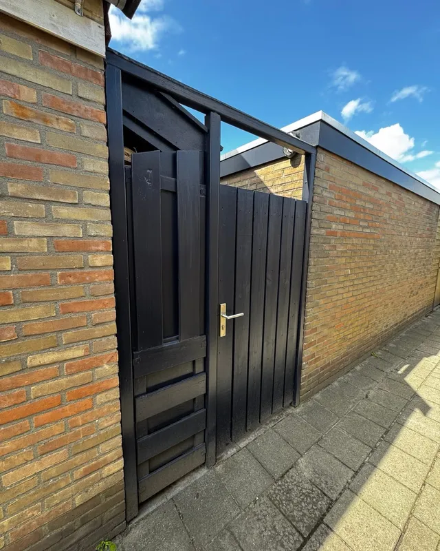 Nieuwe zwarte dubbele poort tussen twee bakstenen muren, met een blauwe lucht erboven