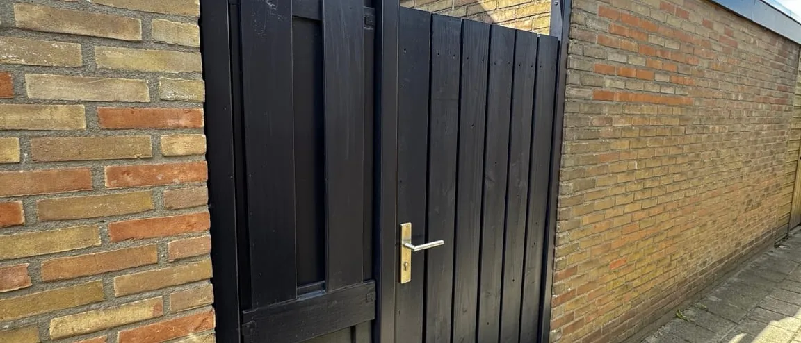 Nieuwe zwarte dubbele poort tussen twee bakstenen muren, met een blauwe lucht erboven
