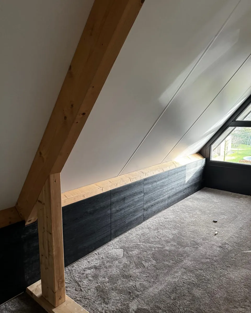 Afgewerkte zolderkamer met een wit schuin dak, houten balken en een donker betimmerd knieschot
