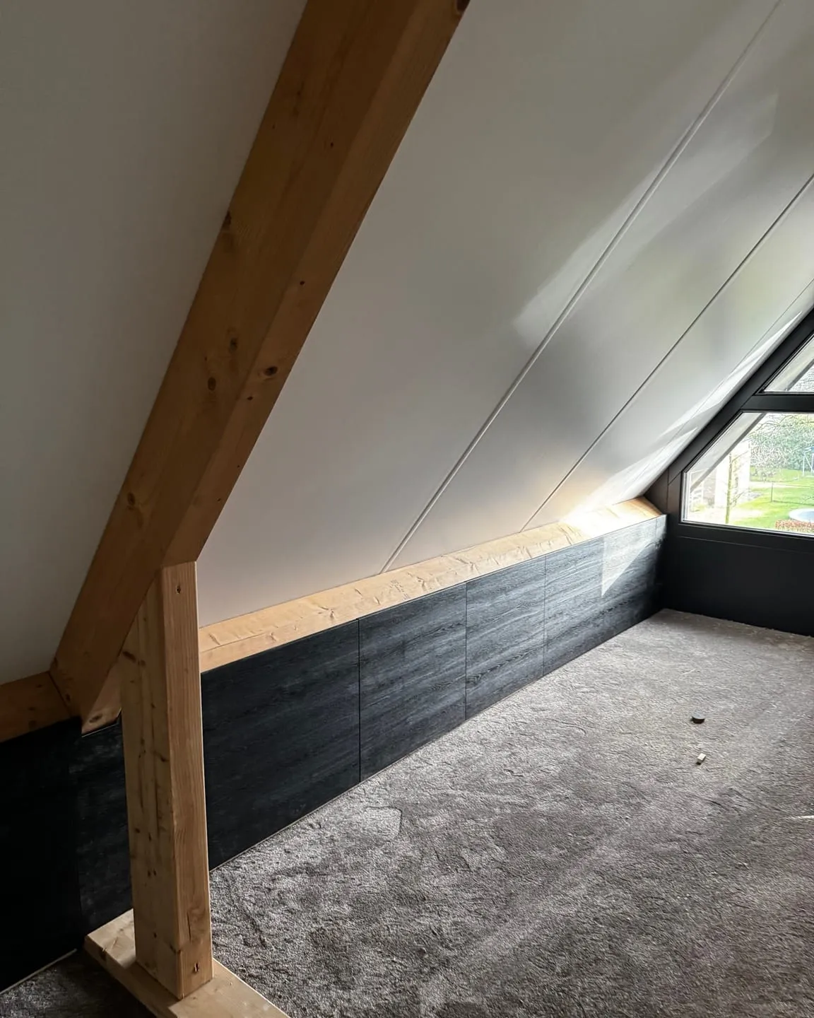 Afgewerkte zolderkamer met een wit schuin dak, houten balken en een donker betimmerd knieschot