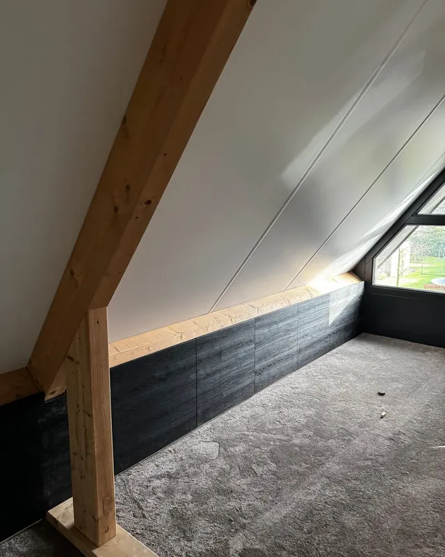 Afgewerkte zolderkamer met een wit schuin dak, houten balken en een donker betimmerd knieschot