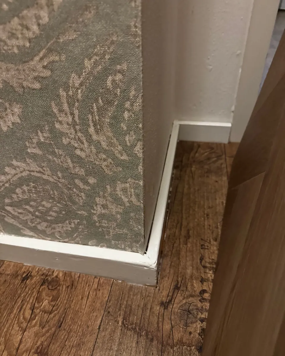Donkere houten vloer met een nieuwe witte plint die strak op de behangen wand aansluit