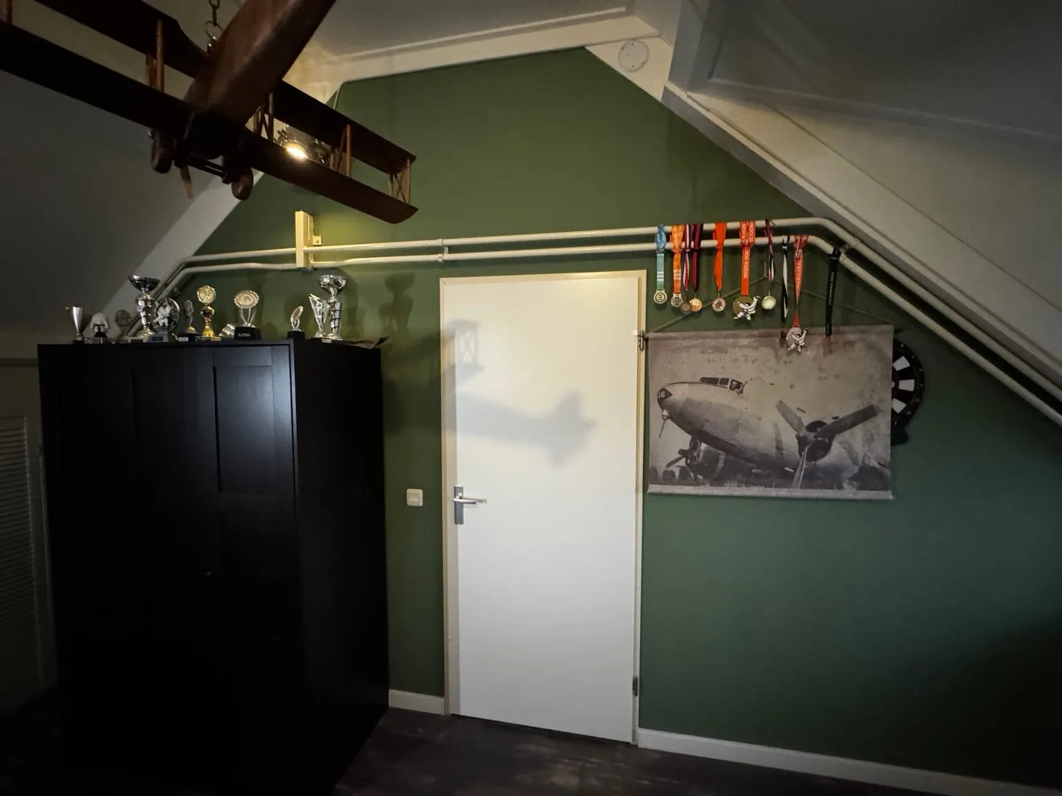 Zolderslaapkamer met een diepgroene wand, een witte deur en een donkere kast onder het schuine dak