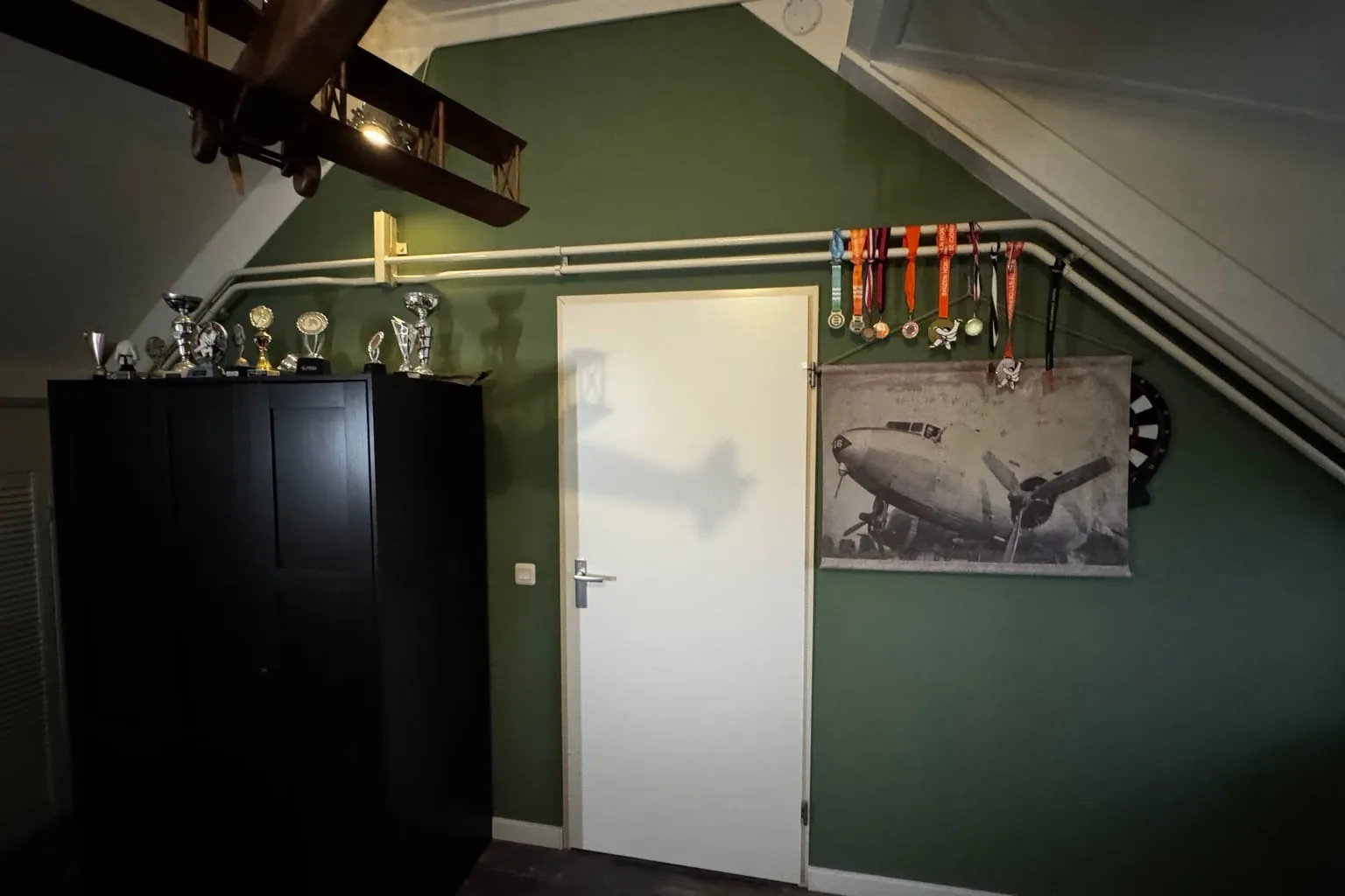 Zolderslaapkamer met een diepgroene wand, een witte deur en een donkere kast