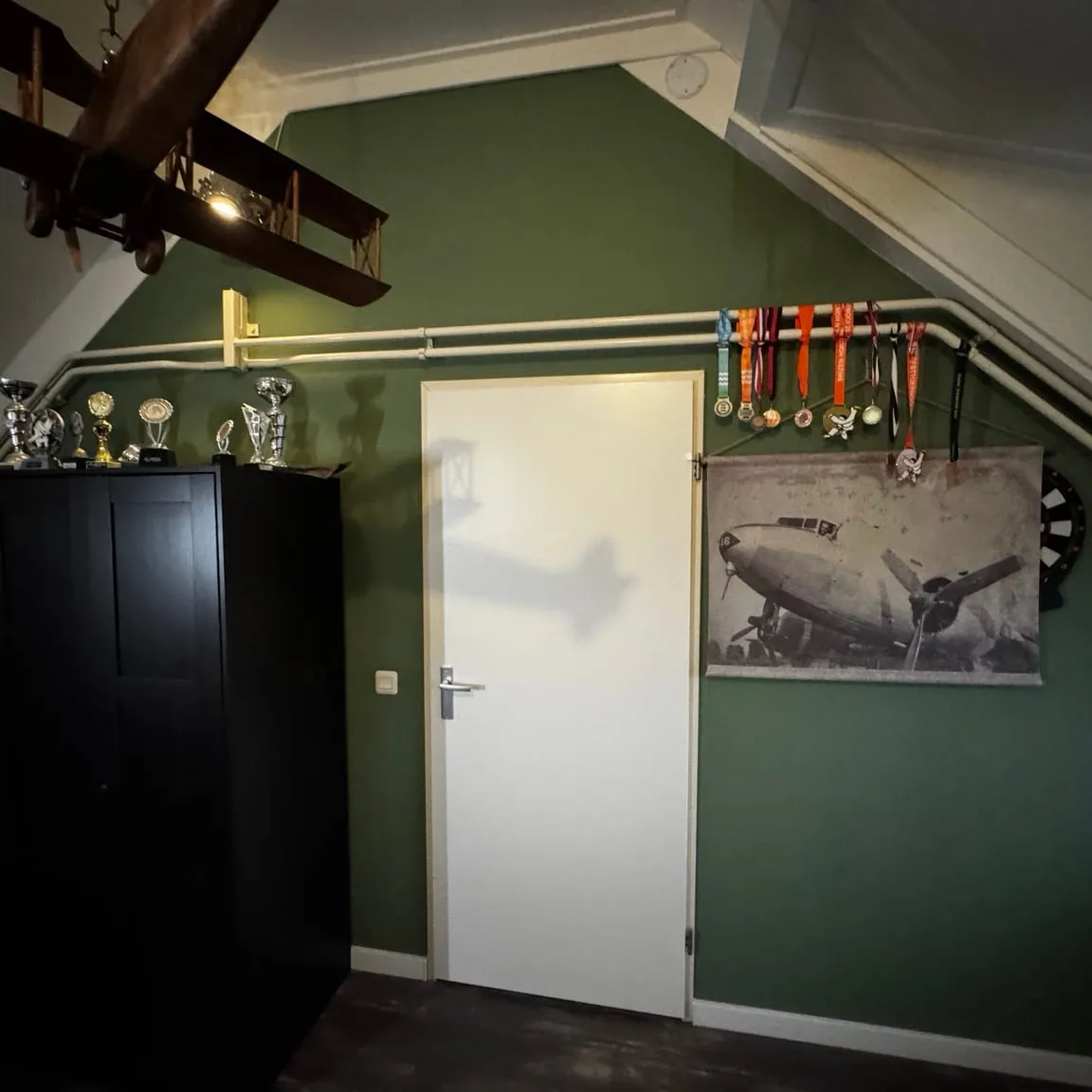 Zolderslaapkamer met een diepgroene wand, een witte deur en een donkere kast onder het schuine dak
