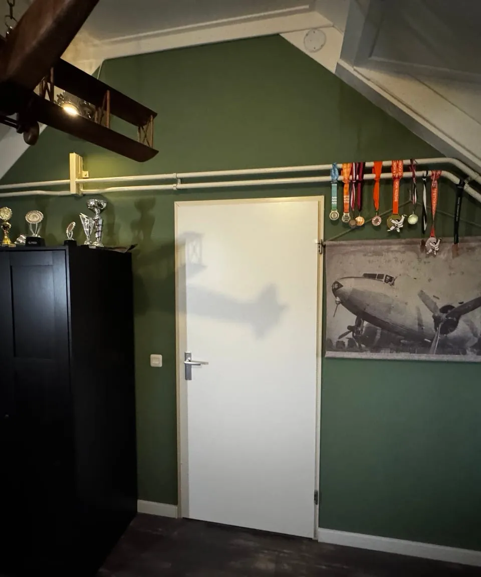 Zolderslaapkamer met een diepgroene wand, een witte deur en een donkere kast onder het schuine dak