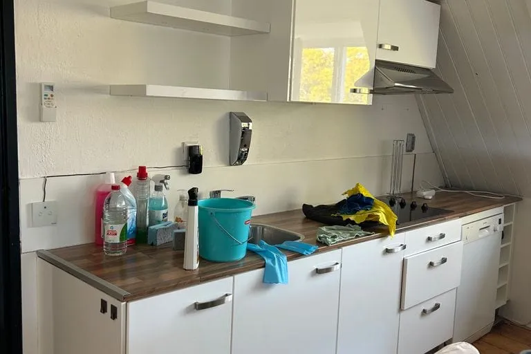De bestaande keuken voor de demontage, met bovenkastjes en een werkblad langs de wand