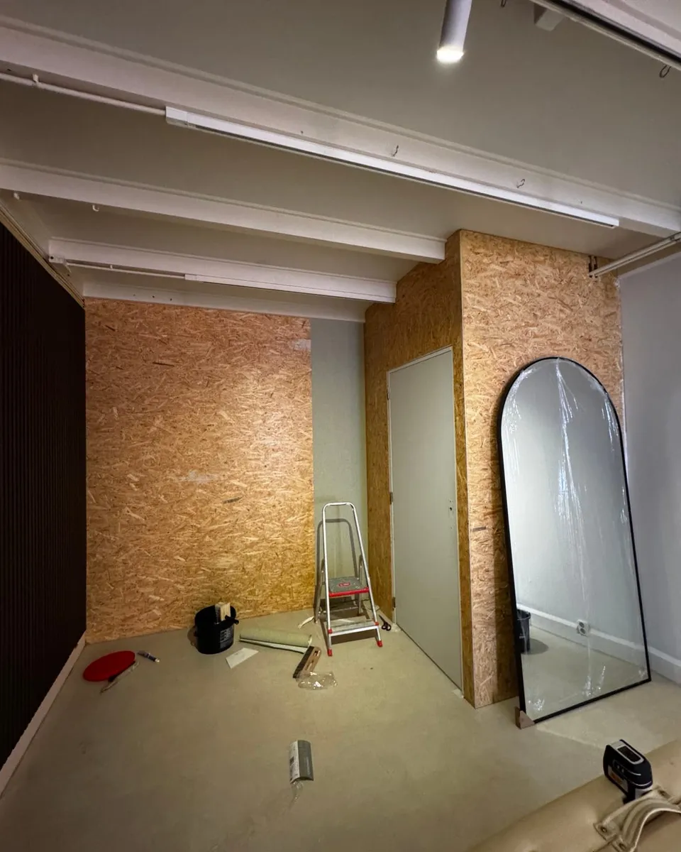 De ruimte voor de renovatie, met onafgewerkte wandplaten, een kale vloer en een ladder