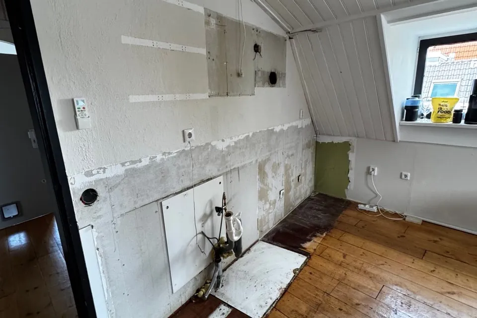 De keukenwand na de demontage, met de leidingen en aansluitingen vrij in het zicht