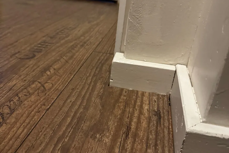 Donkere houten vloer met een nieuwe witte plint die in de hoek op het deurkozijn aansluit
