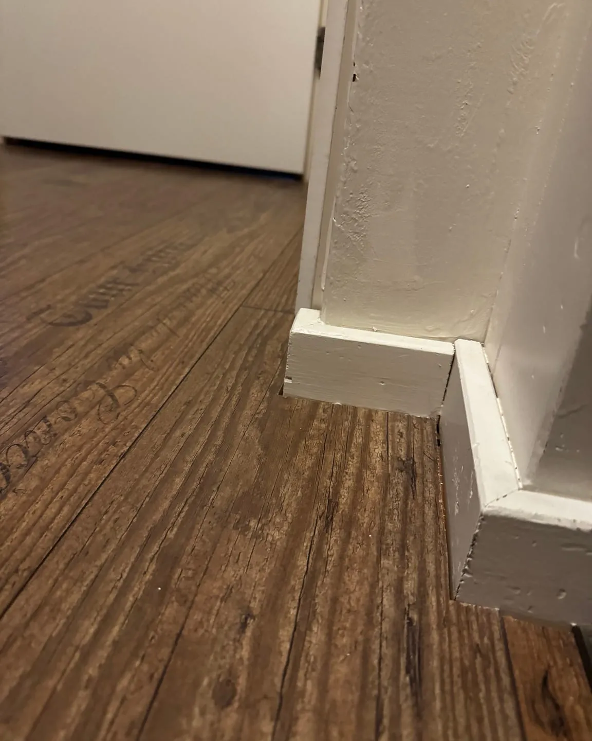 Donkere houten vloer met een nieuwe witte plint die in de hoek op het deurkozijn aansluit