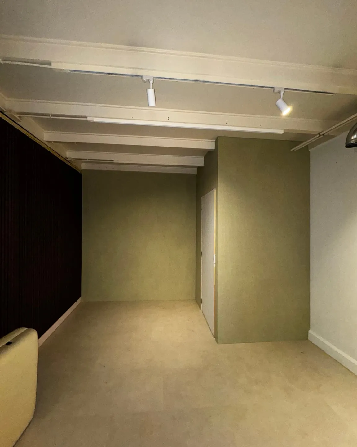 Opgeleverde kamer met zachtgroene wanden, witte plafondbalken en spots aan een rail
