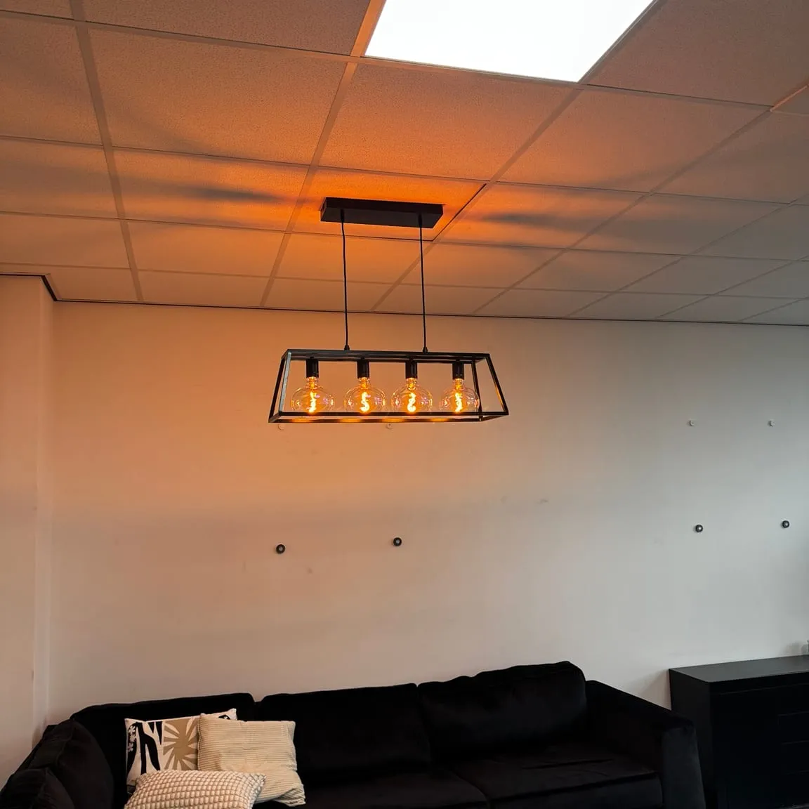 Zwart frame-armatuur met warme lampen boven de zithoek in een kantoorruimte