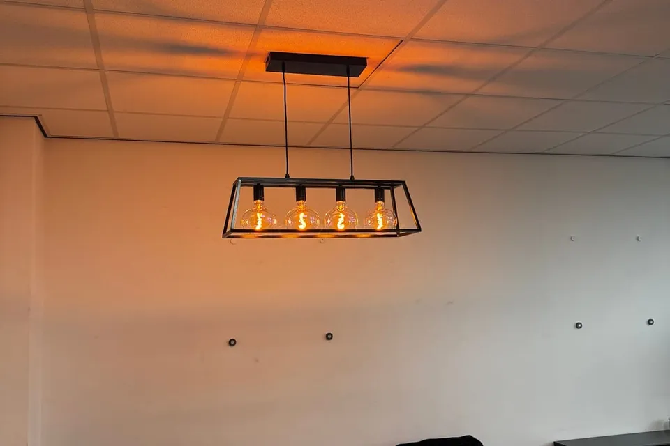 Zwart frame-armatuur met warme lampen boven de zithoek in een kantoorruimte
