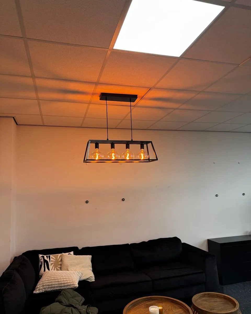 Zwart frame-armatuur met warme lampen boven de zithoek in een kantoorruimte