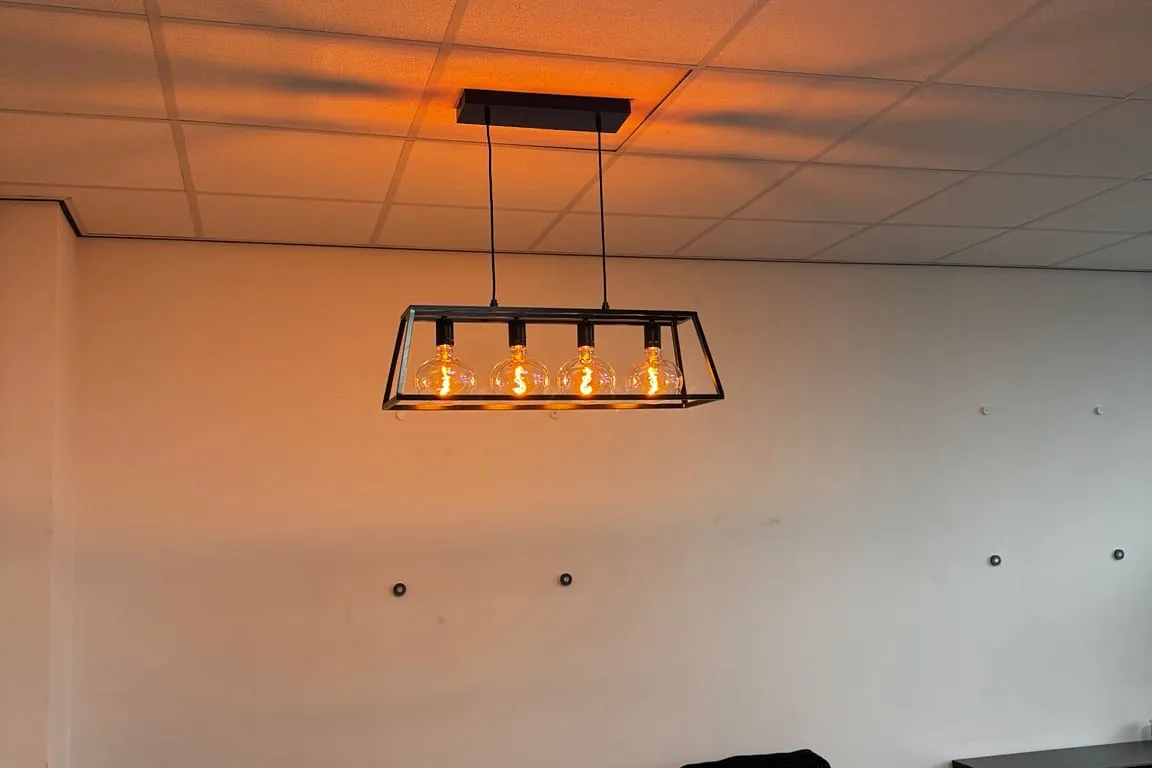Zwart frame-armatuur met warme lampen boven de zithoek in een kantoorruimte