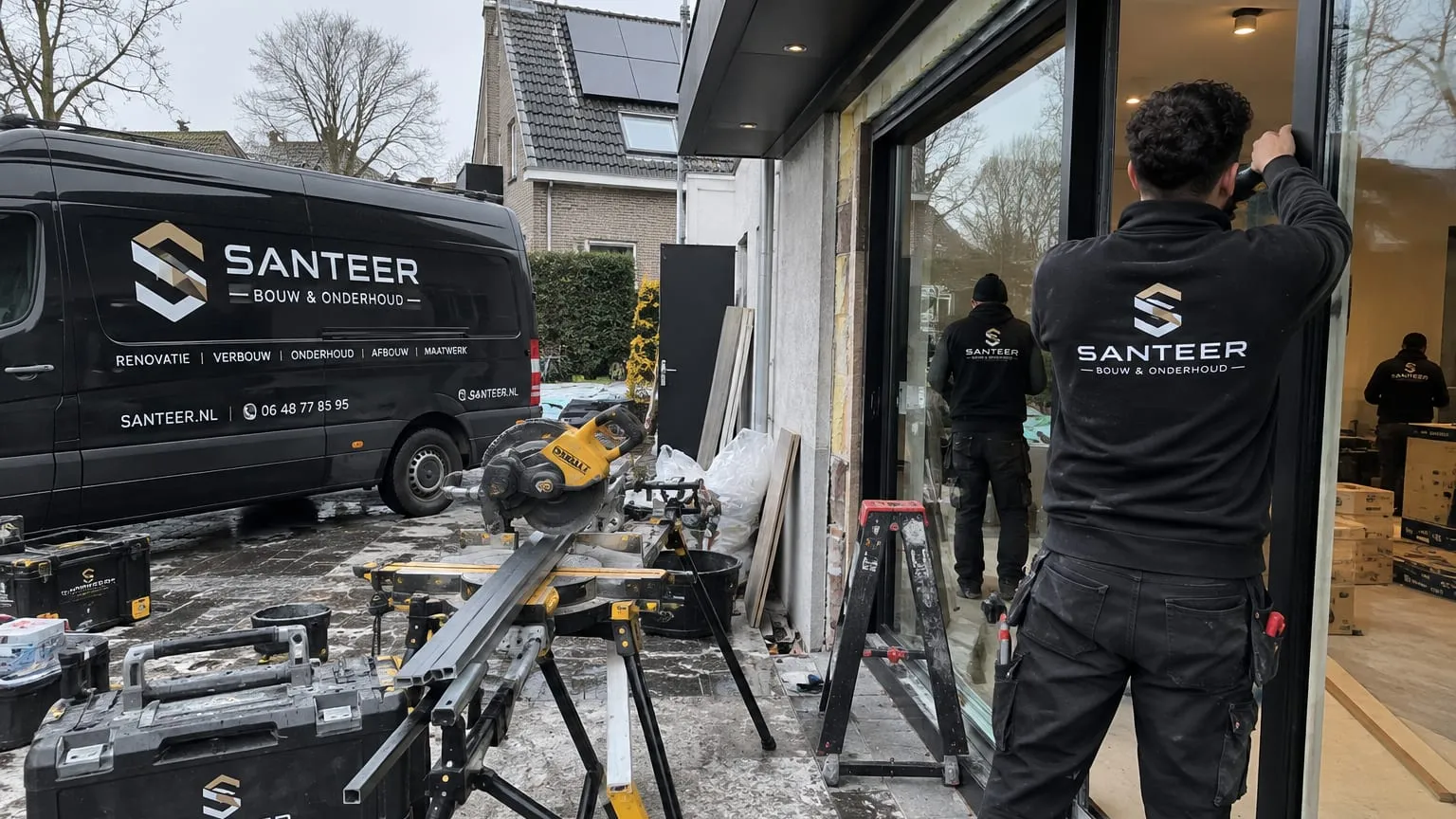 Twee medewerkers van SANTEER plaatsen glas in een schuifpui, met de bedrijfsbussen ervoor